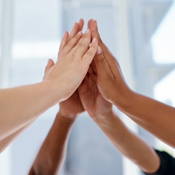 Fünf Hände verschiedener Hauttöne berühren sich in einem positiven Moment des Zusammenhalts und der Zusammenarbeit.