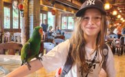 Mädchen zeigt stolz blau-grünen Papagei auf Arm - China for family - China mit Kindern