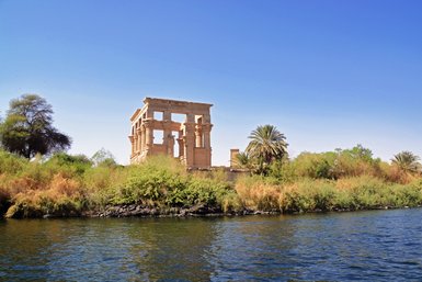 Die ruins of the Philae-Tempel erheben sich majestätisch über das grüne Ufer des Nils, umgeben von üppigem Grün und Palmen.