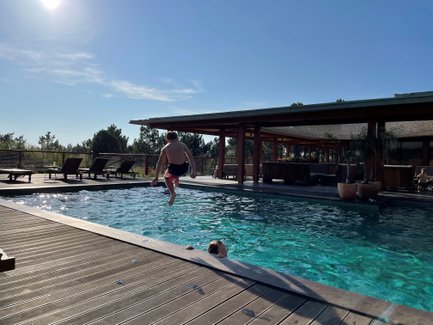 Ein Junge springt fröhlich in einen glitzernden Pool, während ein anderer im Wasser schwimmt und die Sonne scheint.