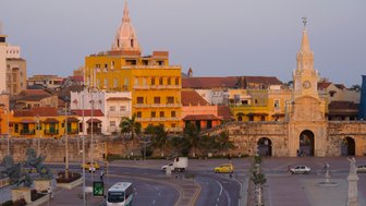 Bunte Gebäude mit historischen Fassaden und einer markanten Kirchturmspitze prägen die Skyline von Cartagena bei Sonnenuntergang.