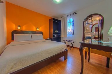 Ein gemütliches Hotelzimmer mit einem großen Bett, orangefarbener Wand und warmem Licht von Wandlampen.
