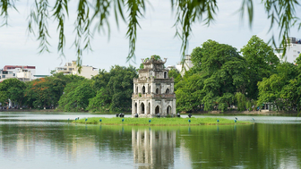 Ein historischer Turm steht auf einer kleinen Insel, umgeben von ruhigem Wasser und üppigem Grün in Hanoi.