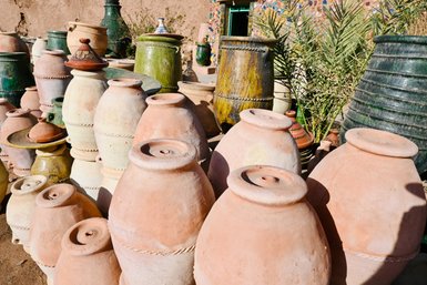 Eine Vielzahl von Tontöpfen in verschiedenen Farben und Größen steht in der Sonne, umgeben von grünen Pflanzen.