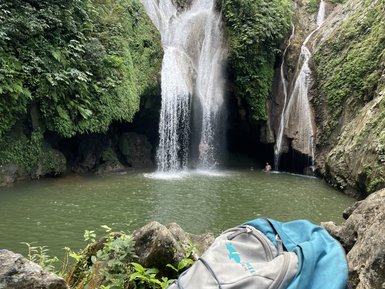 Ein beeindruckender Wasserfall stürzt in einen klaren, grünen Teich, umgeben von üppigem, grünem Laub und Felsen.