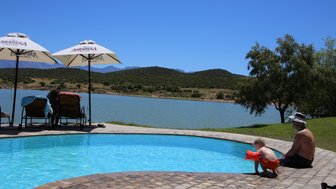 Ein kleiner Junge mit Schwimmflügeln beugt sich über den Rand eines Pools, während ein Mann entspannt daneben sitzt.
