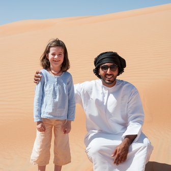 Mädchen steht neben einem Beduinen in der Wüste Omans – Oman mit Kindern