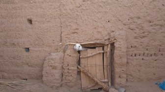 Eine kleine Holztür, die in einer lehmigen Wand eingebaut ist, zeigt einen rustikalen, traditionellen Baustil.