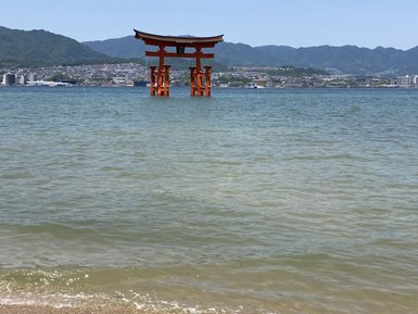 Ein rotes Torii steht majestätisch im Wasser, umgeben von sanften Wellen und einer malerischen Berglandschaft im Hintergrund.