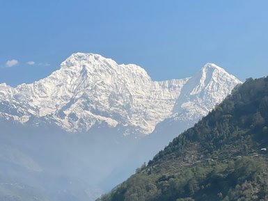 Majestätische schneebedeckte Berge erheben sich über grüne Terrassenfelder, die sanft die Hänge hinunterführen.