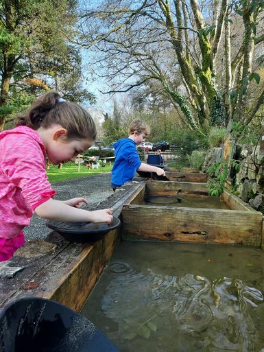 Ein Mädchen und ein Junge stehen an einem Wasserbecken und versuchen, Gold zu schürfen, während die Sonne scheint.