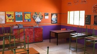 Ein Klassenzimmer mit orangefarbenen Wänden, leeren Tischen und Stühlen, die auf den Tischen stehen, bereit für den Unterricht.