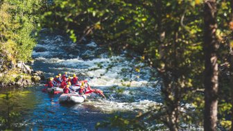 Eine Gruppe von Menschen in roten Schwimmwesten paddelt in einem Schlauchboot auf einem rauschenden Fluss.