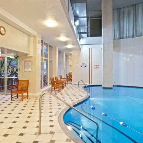 Ein Innenpool mit klarem Wasser, umgeben von hellen Wänden und Holzstühlen, die zum Entspannen einladen.