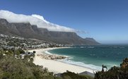 Eine atemberaubende Küstenlandschaft mit sanften Wellen, feinem Sandstrand und majestätischen Bergen im Hintergrund.