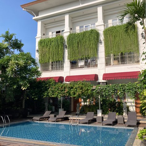 Ein einladender Poolbereich mit Liegen, umgeben von üppigem Grün und einem eleganten Gebäude im Hintergrund.