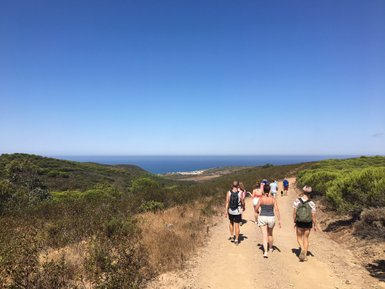 Eine Gruppe von Wanderern genießt einen sonnigen Tag auf einem Pfad mit Blick auf das Meer und die umliegenden Hügel.