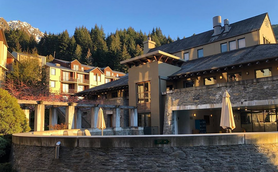 Das Heritage Hotel in Queenstown zeigt eine moderne Architektur, umgeben von üppigem Grün und majestätischen Bergen im Hintergrund.