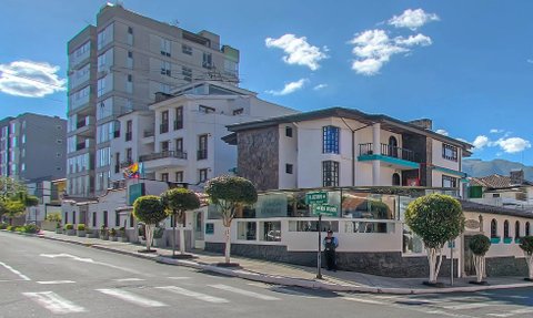 Ein modernes Hotelgebäude mit einer Steinfassade und bunten Fenstern, umgeben von gepflegten Bäumen und einer klaren blauen Himmel.