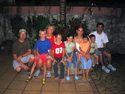 Eine Gruppe von fünf Kindern und vier Erwachsenen posiert fröhlich vor einer grünen Pflanzenwand in einem Innenhof.