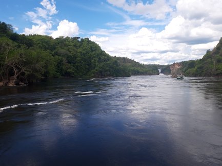 Ein ruhiger Fluss schlängelt sich durch üppige grüne Hügel, während Wolken am blauen Himmel vorbeiziehen.