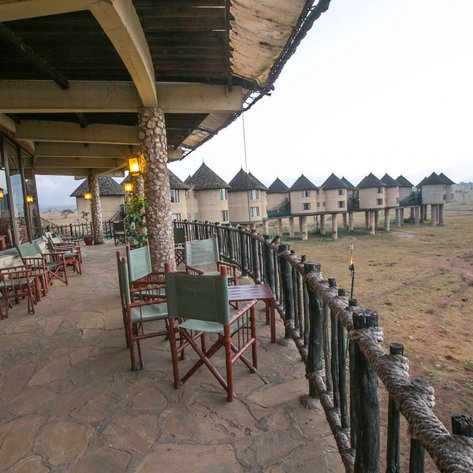 Eine Terrasse mit Holzstühlen und Tischen bietet einen Blick auf die Taita Hills und die umliegende Landschaft.
