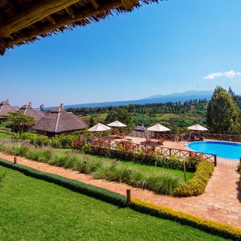 Ein atemberaubender Blick auf den Pool des Neptune Ngorongoro Lodges, umgeben von üppigem Grün und Bergen im Hintergrund.