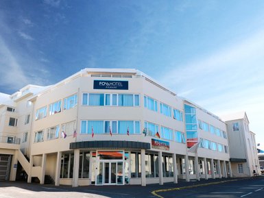 Das Fosshotel Raudara präsentiert sich mit einer modernen Fassade und großen Fenstern unter einem strahlend blauen Himmel.
