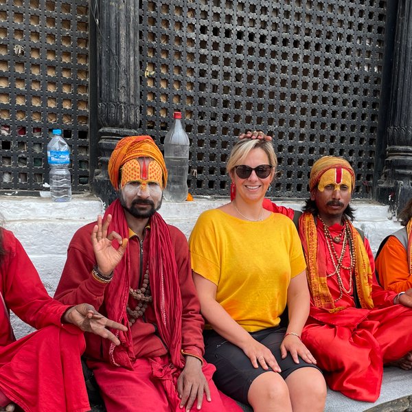 Eine Frau in gelbem Shirt sitzt mit vier farbenfroh gekleideten Männern, die traditionelle Gesichtsbemalung tragen, auf einer Treppe.