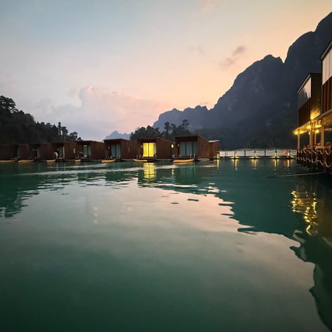 Ein ruhiger Abendblick auf ein schwimmendes Resort, umgeben von Bergen und spiegelndem Wasser, das sanft im Licht schimmert.