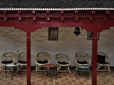 Eine gemütliche Veranda mit mehreren Rattanstühlen und kleinen Tischen, umgeben von einer weißen Wand und einem roten Dach.