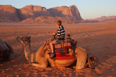 Kind sitzt beim Sonnenuntergang auf einem Kamel - Jordanien mit Kindern