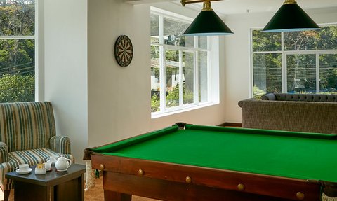 Ein heller Raum mit einem Billardtisch, gemütlichen Sesseln und großen Fenstern, die einen Blick auf die grüne Landschaft bieten.