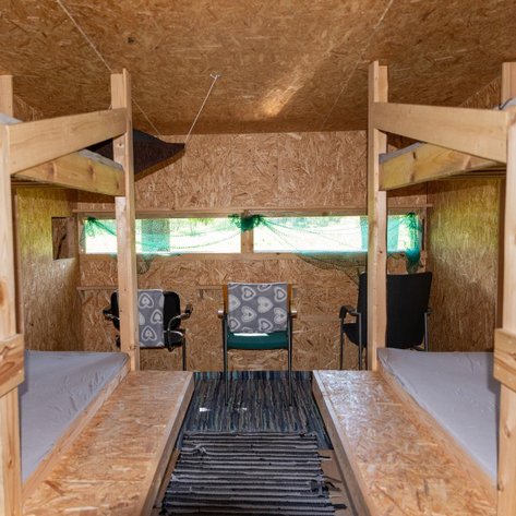 Der Innenraum einer Holzhütte mit zwei Etagenbetten und Stühlen, ideal für Beobachtungen in der Natur.