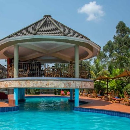 Ein einladender Poolbereich mit einem überdachten Pavillon und Liegen, umgeben von üppigem Grün und strahlend blauem Himmel.