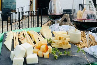 Ein rustikales Käsebrett mit verschiedenen Käsesorten, Brotsticks und Rotwein, umgeben von einer malerischen Kulisse.