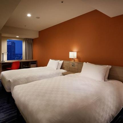 Ein modernes Hotelzimmer mit zwei Einzelbetten, einem Schreibtisch und einem großen Fenster, das auf die Stadt blickt.