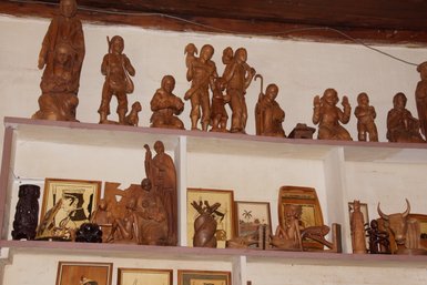 Eine Sammlung von kunstvoll geschnitzten Holzfiguren, die verschiedene Szenen und Charaktere darstellen, auf einem Regal angeordnet.