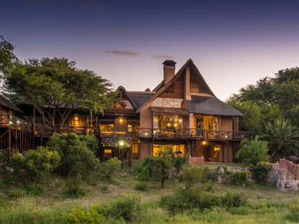 Ein elegantes Safari-Lodge-Gebäude mit Holzveranda, umgeben von üppigem Grün und sanften Hügeln im Abendlicht.