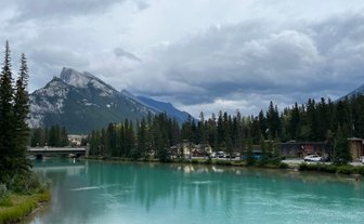 Ein ruhiger Fluss mit türkisfarbenem Wasser fließt durch eine bewaldete Landschaft, umgeben von majestätischen Bergen.