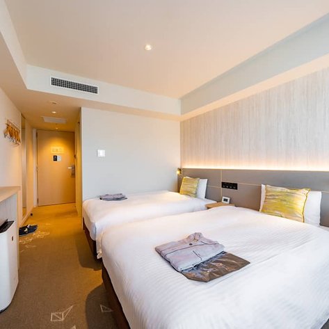 Ein modernes Hotelzimmer mit zwei Einzelbetten, einem Fernseher und einem warmen, einladenden Ambiente.