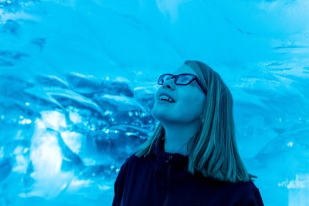 Ein Mädchen mit Brille lächelt begeistert, während sie unter einer blauen Eisdecke steht, die Licht reflektiert.