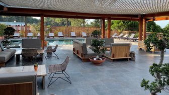 Ein eleganter Außenbereich mit modernen Möbeln, umgeben von Pflanzen und einem glitzernden Pool im Hintergrund.