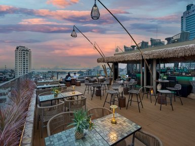 Eine stilvolle Dachterrasse mit modernen Möbeln, umgeben von Pflanzen und einem atemberaubenden Sonnenuntergang über der Stadt.