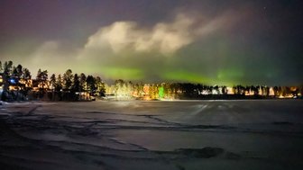 Ein winterlicher See unter einem sternenklaren Himmel, beleuchtet von den tanzenden Lichtern des Nordlichts.