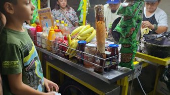 Ein Junge steht an einem bunten Straßenstand, der mit Snacks, Getränken und frischen Früchten gefüllt ist.