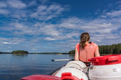 Eine Person sitzt in einem Kanu und blickt auf einen ruhigen See, umgeben von üppigen Wäldern und einem strahlend blauen Himmel.