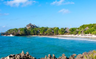 Ein malerischer Blick auf die Küste von Chale Island mit sanften Wellen und üppiger Vegetation im Hintergrund.