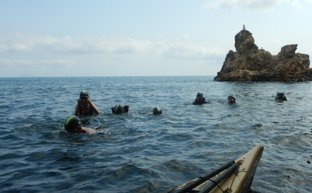 Eine Gruppe von Schwimmern erkundet das klare Wasser, während ein Kajak im Vordergrund liegt und Felsen im Hintergrund sichtbar sind.