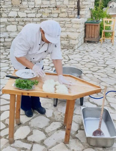 Eine Person in Kochkleidung bereitet frischen Halloumi-Käse auf einem Holztisch im Freien vor.